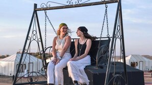 Two people sitting on a swing with a metal frame and chains. - Merzouga Luxury Camp (Taouz)