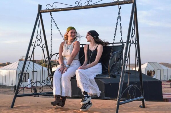 Two people sitting on a swing with a metal frame and chains. - Merzouga Luxury Camp (Taouz)