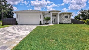 A modern two-story house with a garage, a stone accent wall, and a well-maintained lawn. - Modern Vacation Home Fully Fences Near Airport (Lehigh Acres)