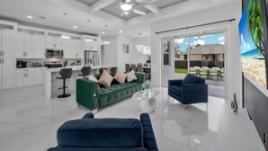 A modern living room with a green sofa, a blue armchair, and a glass coffee table. - Modern Vacation Home Fully Fences Near Airport (Lehigh Acres)