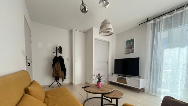Un salon moderne avec un canapé, une table basse, un téléviseur et un porte-manteau.