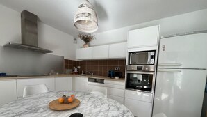 Une cuisine moderne avec des armoires blanches, un four encastré, un four à micro-ondes et une hotte de cuisine en acier inoxydable.