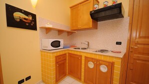 A compact kitchen with yellow tiles, wooden cabinets, a microwave, a sink, and a small shelf with jars.