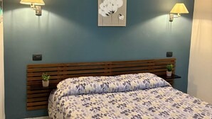 A bedroom with a bed, two wall-mounted lamps, a wall art piece, and a wooden headboard.
