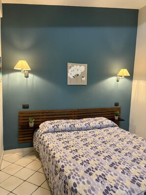 A bedroom with a bed, two wall-mounted lamps, a wall art piece, and a wooden headboard.