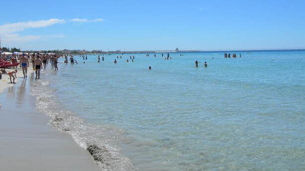 A beach with clear water and people swimming and walking along the shore.