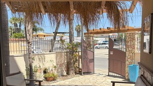 A covered patio area with a seating arrangement, a stone floor, and a view of the street and parked cars.