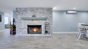 Una sala moderna con chimenea de piedra, un comedor con sillas blancas y una unidad de aire acondicionado visible.