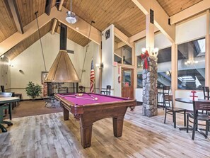 A spacious room with a pool table, wooden flooring, and a stone fireplace. - Woodsy A-Frame in Pocono Mountain Resort, Family and Pet Friendly! (Gouldsboro)