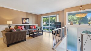 A living room with a sofa, coffee table, and a TV. There is a window with a view of the outdoors. - Spacious 5-Bedroom House in Rockville Fast WiFi, Gaming Area & Fenced Yard (Rockville)