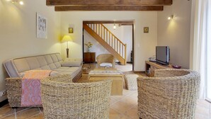 Ein gemütliches Wohnzimmer mit einer Couch, Korbstühlen, einem Couchtisch, einem Fernseher und einer Treppe, die in einen anderen Raum führt.