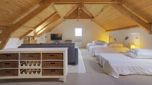 Ein Zimmer mit hohen Decken, sichtbarer Holzträgerkonstruktion, einem Fernseher, zwei Betten, einem Sofa und Korbo-Aufbewahrung.