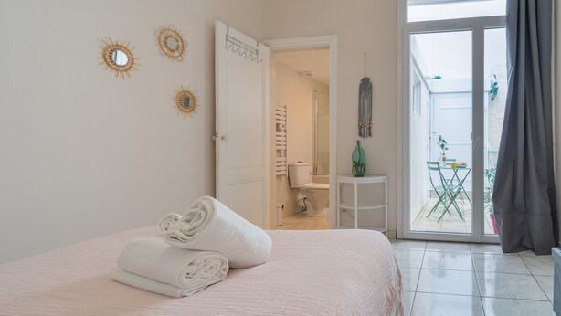 A bedroom with a bed, a bathroom visible through an open door, and a balcony with a table and chairs. - Arca Day - Appt 4p à Arcachon proche dune du pilat (Arcachon)