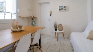 A room with a wooden dining table, white chairs, a white sofa, a small side table with a plant, and a white door. - Arca Day - Appt 4p à Arcachon proche dune du pilat (Arcachon)