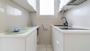 A compact kitchen with white cabinets, a window, a sink, and a small toy van on the counter. - Arca Day - Appt 4p à Arcachon proche dune du pilat (Arcachon)