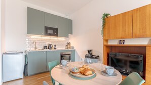 Une cuisine compacte équipée d’un four à micro-ondes, d’un four et d’un évier. On y trouve une table à manger avec des chaises et un petit téléviseur.