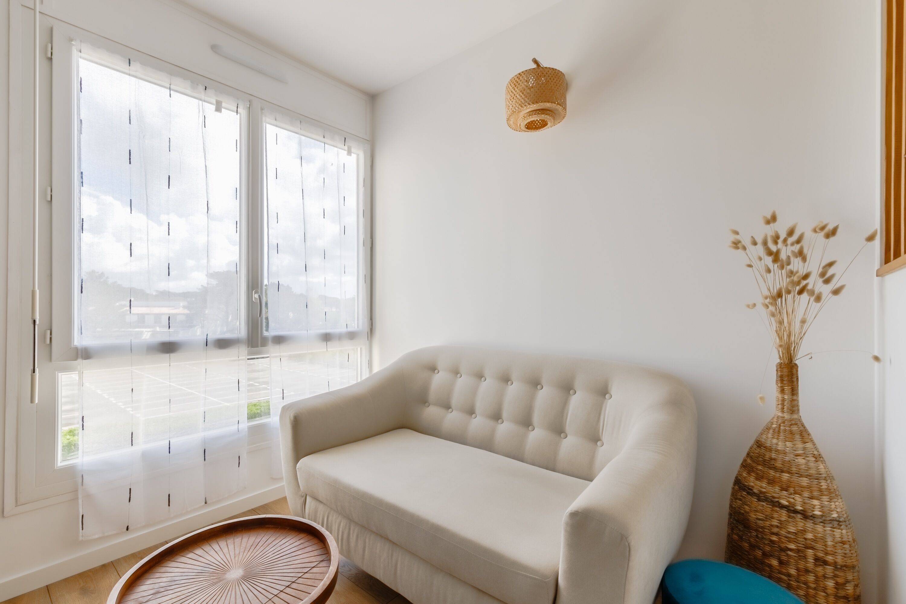 A room with a white sofa, a wicker vase, and a wicker side table.
