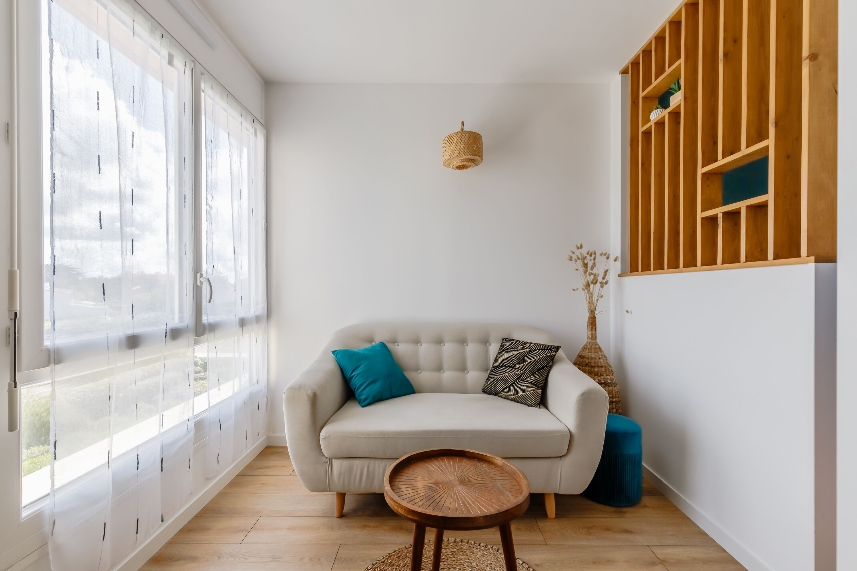 Een kamer met een bank, een klein rond tafeltje, een hanglamp en een houten wandplank.