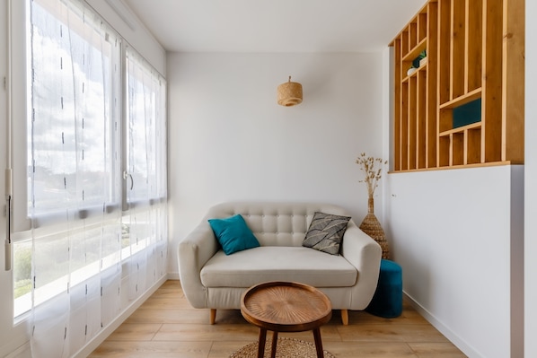 Una habitación con sofá, una mesita redonda, una lámpara colgante y una estantería de madera.
