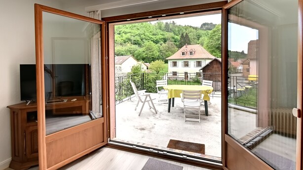 A room with a sliding glass door leading to an outdoor patio with a table and chairs. - Vert Olive - Maison proche Sélestat, Colmar (Rombach-le-Franc)