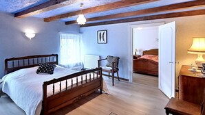 A bedroom with a wooden bed, a chair, a bedside table, and a door leading to another room. - Vert Olive - Maison proche Sélestat, Colmar (Rombach-le-Franc)