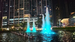 A nighttime view of a cityscape with a water fountain in the foreground and modern buildings in the background. - Luxury Upscale Retreat in Uptown Bgc, Metro Manila (Taguig)