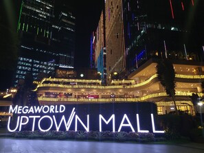 The exterior of the Uptown Mall with illuminated signage and surrounding high-rise buildings. - Luxury Upscale Retreat in Uptown Bgc, Metro Manila (Taguig)
