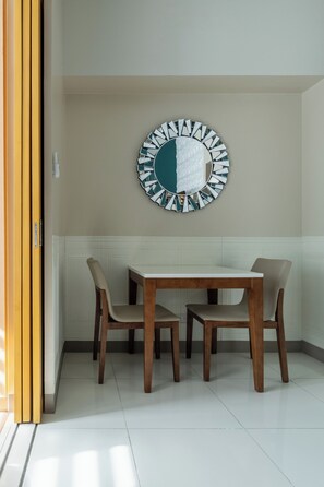 A dining area with a round mirror on the wall, a wooden table, and two chairs. - Luxury Upscale Retreat in Uptown Bgc, Metro Manila (Taguig)