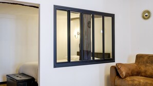 A room with a bed, a window, a brown sofa, and a small stool. - Le Turbiasque - apt climatisé - 500m de la plage (La Turbie)