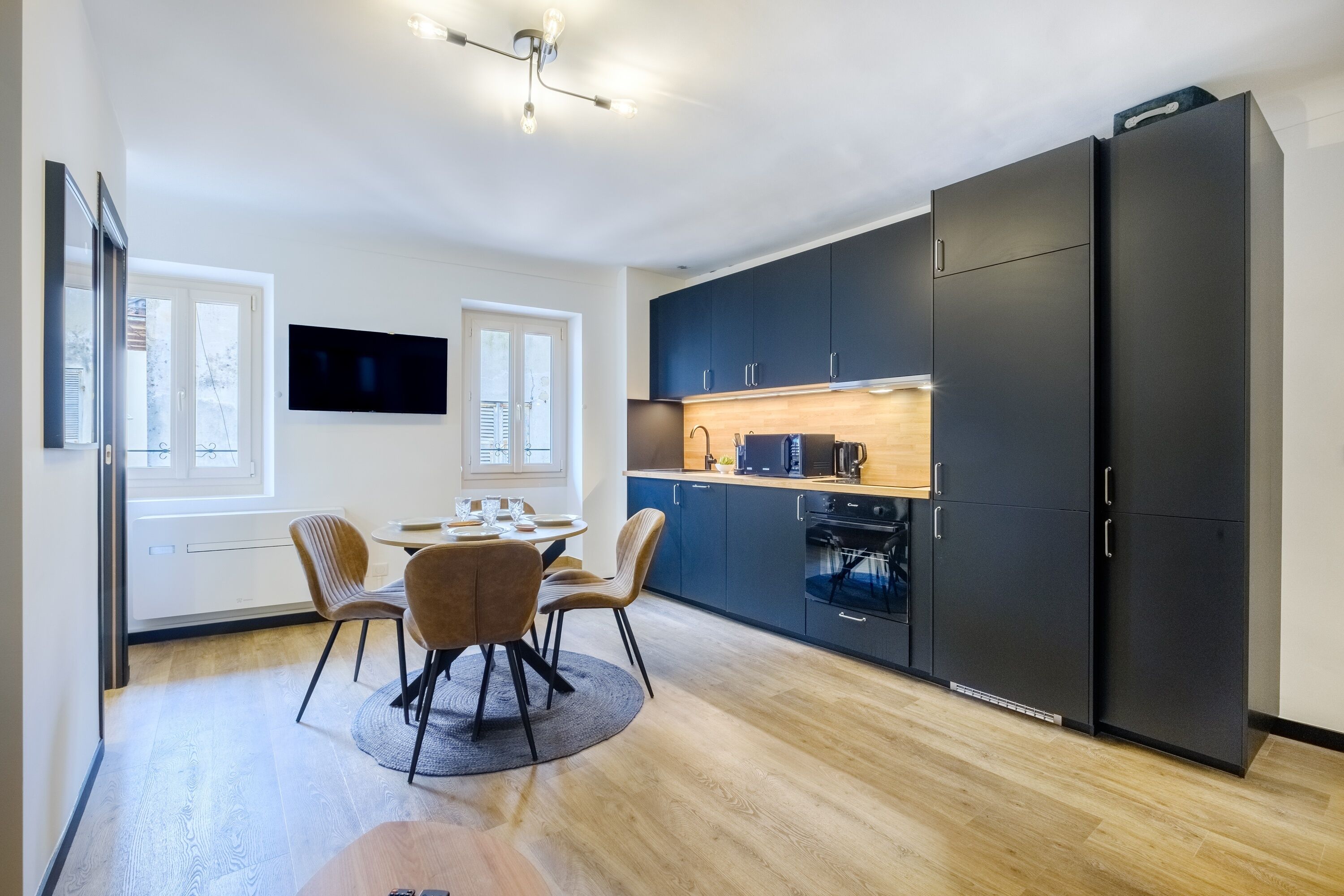 Une cuisine moderne avec des meubles de couleur sombre, un four à micro-ondes et une machine à café. Un coin repas est aménagé avec une table et des chaises.