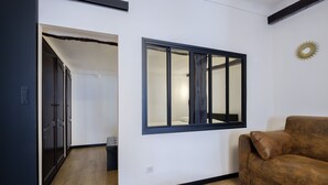 A room with a brown sofa, a wooden bench, a window with blinds, and a dark wooden door. - Le Turbiasque - apt climatisé - 500m de la plage (La Turbie)