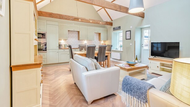 A spacious living area with a high ceiling, wooden beams, a dining table with chairs, a sofa, a television, and a kitchen in the background. - 2 bedroom accommodation in Ayr (Ayr)
