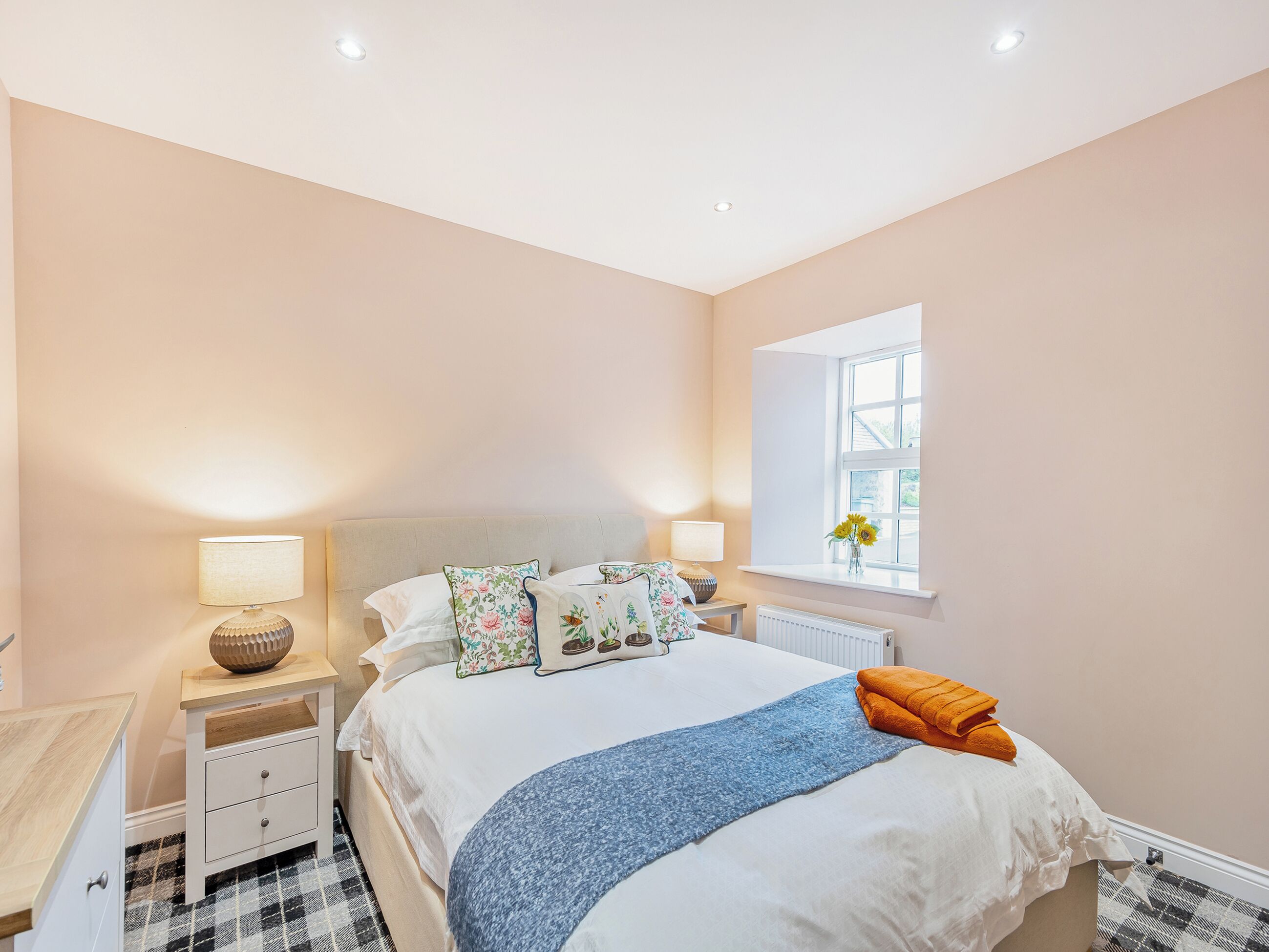 A neatly arranged bedroom with a bed, bedside tables, a window with a view, and a radiator.