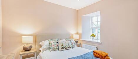 A neatly arranged bedroom with a bed, bedside tables, a window with a view, and a radiator.
