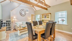 A spacious living area with a high ceiling, wooden beams, a dining table with chairs, a sofa, a coffee table, and a bookshelf. - 2 bedroom accommodation in Ayr (Ayr)