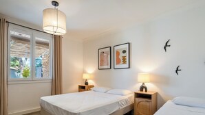 Hotellihuone, jossa on kaksi sänkyä, suuri ikkuna verhoilla, riippuvalaisin ja taideteoksia seinillä.