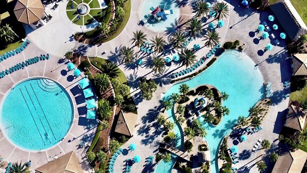 Vue aérienne d’un complexe hôtelier doté de plusieurs piscines, d’espaces de détente et de palmiers.