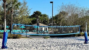 Un filet de volley-ball de plage, des chaises longues bleues et un bâtiment en arrière-plan.