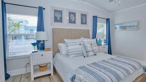 Une chambre à coucher comprenant un lit, des tables de chevet, un ventilateur de plafond et des œuvres d’art encadrées accrochées au mur.