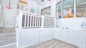 Une chambre décorée sur le thème de la marine, avec un plancher en bois blanc, un ventilateur de plafond et une fenêtre donnant sur l’extérieur.