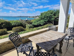 Un patio al aire libre con una mesa y sillas, con vistas a un paisaje costero con árboles y el mar.