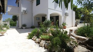 A white building with a stone-paved courtyard, potted plants, and a small garden area. - Villa Lapis Vis - Treat yourself with the vacation you deserve! (Rukavac)