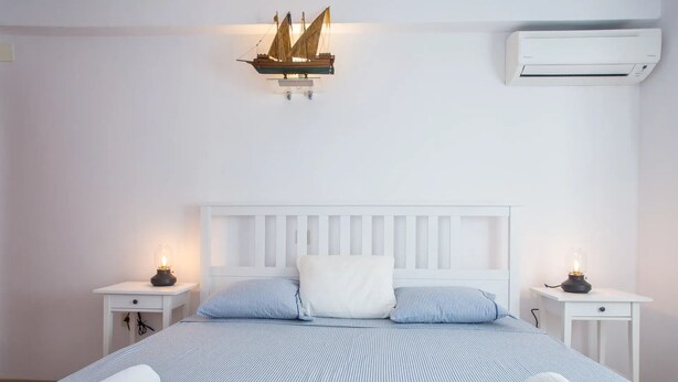 A neatly made bed with striped bedding, two bedside lamps, a white headboard, and a wall-mounted ship model. - Villa Lapis Vis - Treat yourself with the vacation you deserve! (Rukavac)