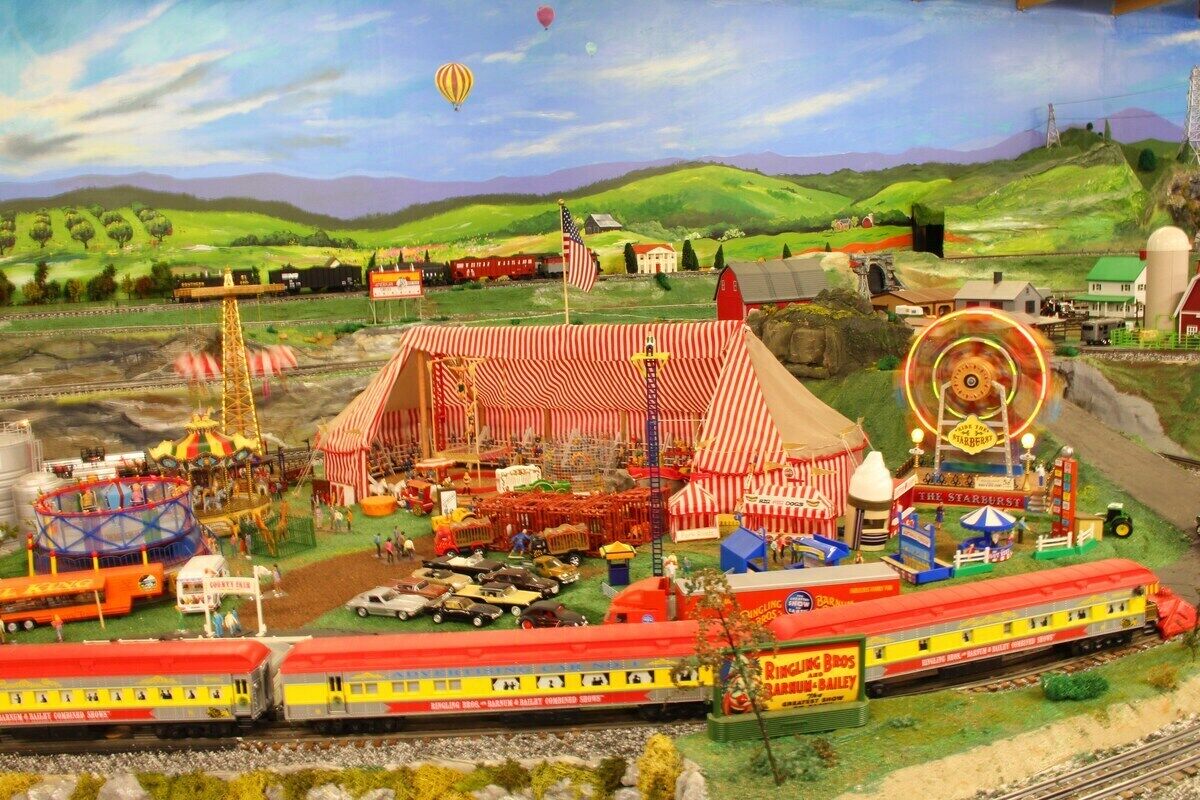A detailed model train layout with a barn, a carousel, and a train station.