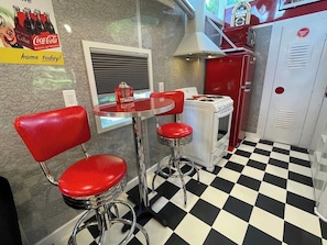A retro diner-style kitchen with a checkered floor, red bar stools, a vintage stove, and a Coca-Cola advertisement. - Mo-Pac Couples Caboose: see bison out in front! (Clyde)