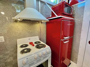 A compact kitchen with a white stove, red refrigerator, and a microwave on top. - Mo-Pac Couples Caboose: see bison out in front! (Clyde)