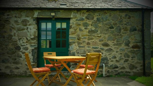 Un edificio de piedra con una puerta verde y una mesa de madera con sillas.