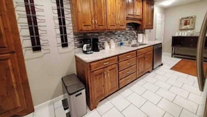A kitchen with wooden cabinets, a granite countertop, a coffee maker, and a trash can.