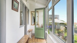 Un pasillo con un banco de madera, una puerta verde y amplios ventanales que dan al exterior.