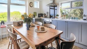 Una cocina moderna con una mesa de comedor de madera, armarios grises y vistas a zonas verdes.